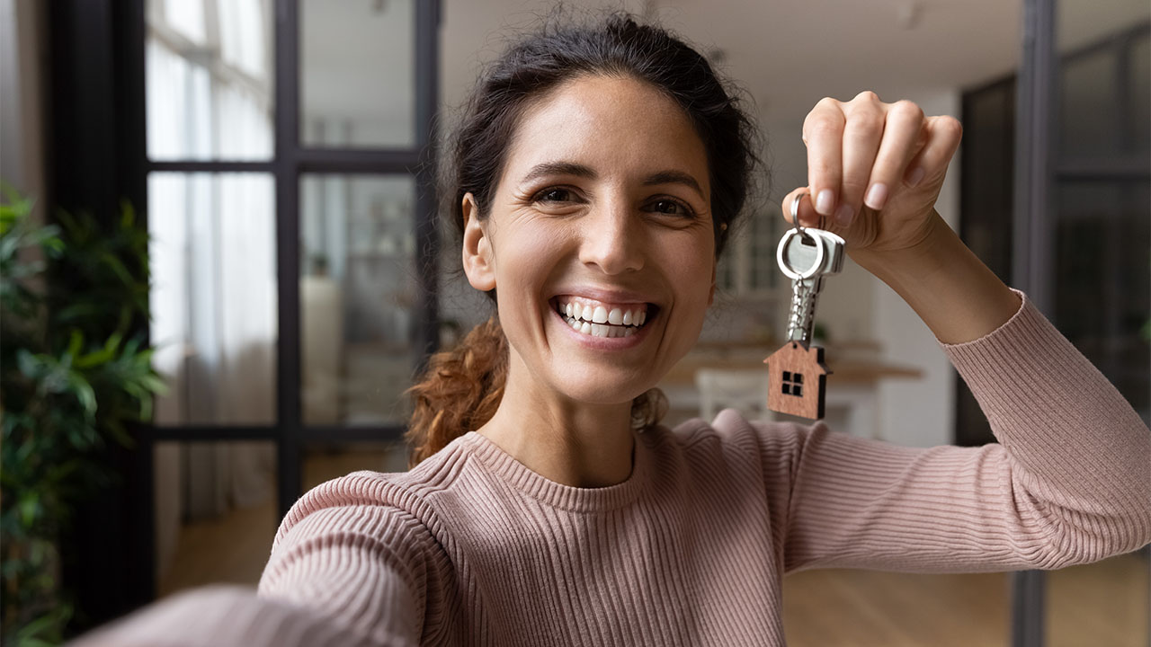 mulher orgulhosa mostrando chave da nova casa, na matéria "Comece o ano planejando a compra da casa própria"